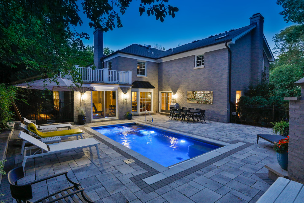 Modelo de casa de la piscina y piscina alargada clásica pequeña rectangular en patio trasero con adoquines de hormigón