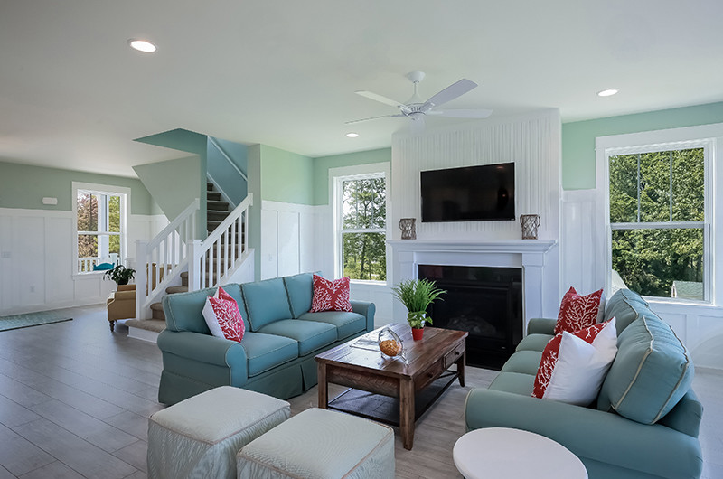 Inspiration for a mid-sized beach style open concept family room in Other with light hardwood floors, a standard fireplace, a wood fireplace surround, green walls, a wall-mounted tv and grey floor.