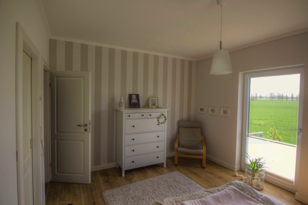 Small country master bedroom in Berlin with beige walls, medium hardwood floors, no fireplace, brown floor and wallpaper.