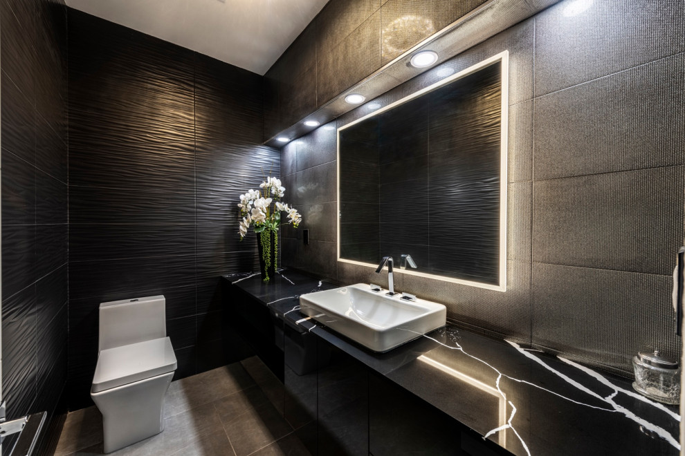This is an example of a large contemporary cloakroom in Las Vegas with flat-panel cabinets, black cabinets, a one-piece toilet, grey tiles, ceramic tiles, black walls, ceramic flooring, a built-in sink, granite worktops, grey floors, black worktops and a floating vanity unit.