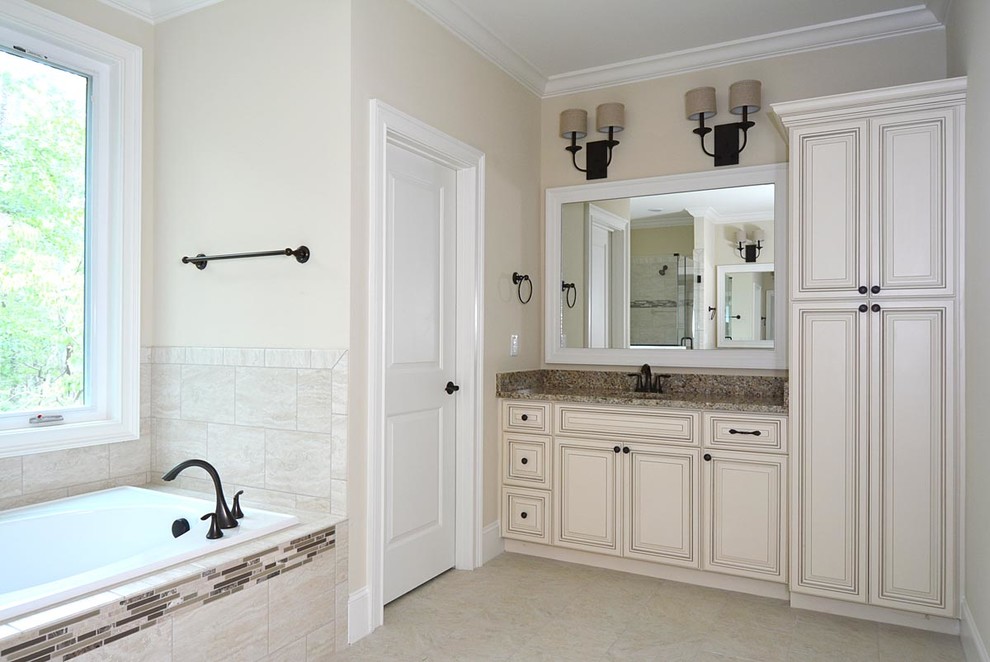 This is an example of a large traditional master bathroom in Raleigh with an undermount sink, raised-panel cabinets, beige cabinets, granite benchtops, a drop-in tub, an alcove shower, a two-piece toilet, multi-coloured tile, ceramic tile, beige walls and ceramic floors.