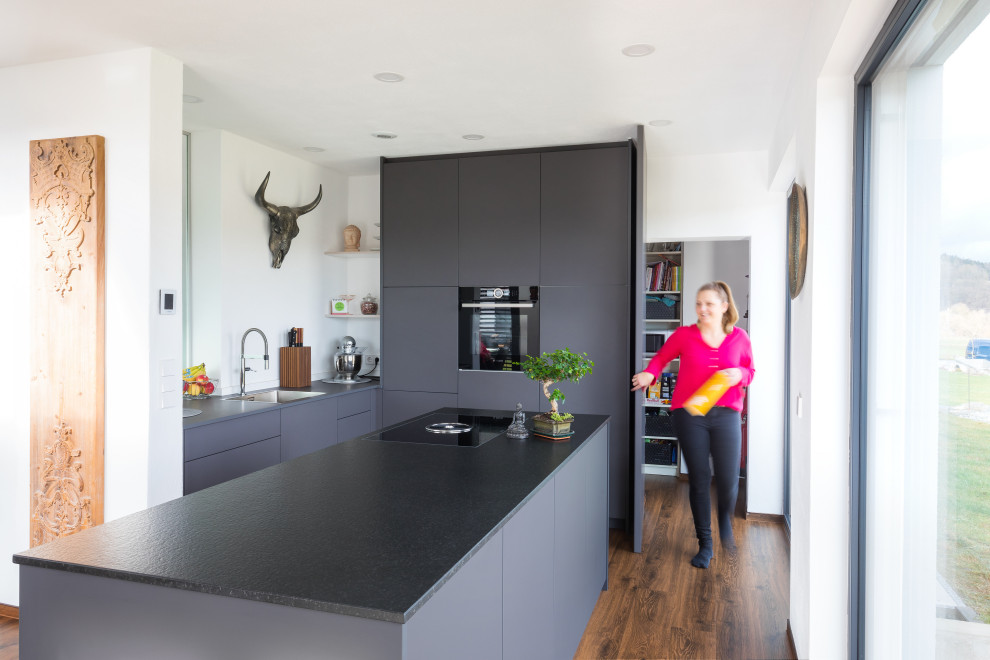 Inspiration for a mid-sized contemporary galley open plan kitchen in Stuttgart with grey cabinets, granite benchtops, black appliances, dark hardwood floors, with island, blue floor and recessed.