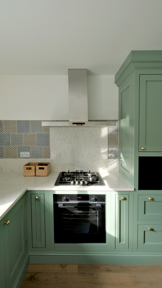 This is an example of a large contemporary l-shaped kitchen/diner in Kent with a built-in sink, shaker cabinets, green cabinets, marble worktops, white splashback, marble splashback, stainless steel appliances, medium hardwood flooring, an island, brown floors, white worktops and feature lighting.