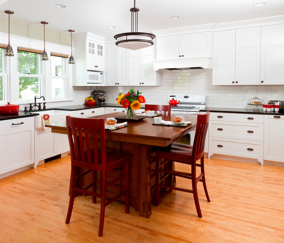Photo of an arts and crafts kitchen in Minneapolis with a farmhouse sink, shaker cabinets, white cabinets, white splashback, subway tile splashback, white appliances and black benchtop.