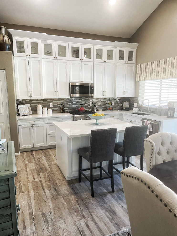 Design ideas for a mid-sized transitional l-shaped open plan kitchen in Phoenix with an undermount sink, shaker cabinets, white cabinets, quartz benchtops, multi-coloured splashback, glass sheet splashback, stainless steel appliances, vinyl floors, with island, beige floor and white benchtop.