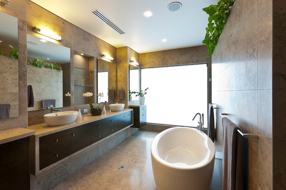 Large modern master bathroom in Perth with a vessel sink, dark wood cabinets, limestone benchtops, a freestanding tub, an alcove shower, beige tile, beige walls and limestone floors.
