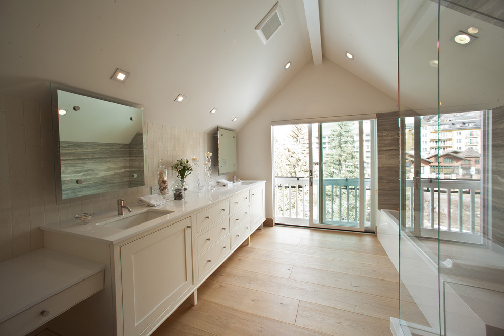 This is an example of a large contemporary master bathroom in Denver with white cabinets, white walls, light hardwood floors, a corner tub, a corner shower, multi-coloured tile, stone slab, an undermount sink, shaker cabinets and marble benchtops.