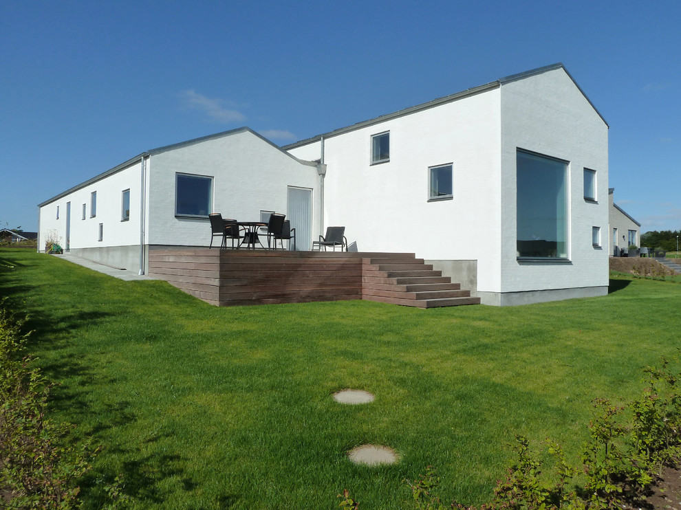 This is an example of a large modern split-level white exterior in Esbjerg with stone veneer and a gable roof.
