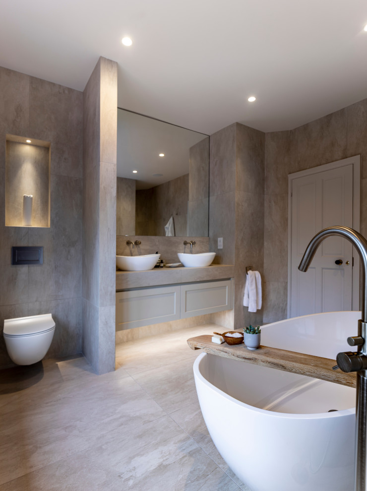 Design ideas for a large contemporary master bathroom in Cheshire with flat-panel cabinets, grey cabinets, a freestanding tub, an open shower, a wall-mount toilet, gray tile, ceramic tile, grey walls, cement tiles, a trough sink, tile benchtops, grey floor, an open shower and grey benchtops.