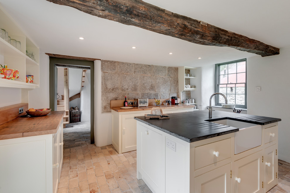 Country u-shaped separate kitchen in Cornwall with a farmhouse sink, shaker cabinets, white cabinets, wood benchtops, brick floors, with island and beige floor.