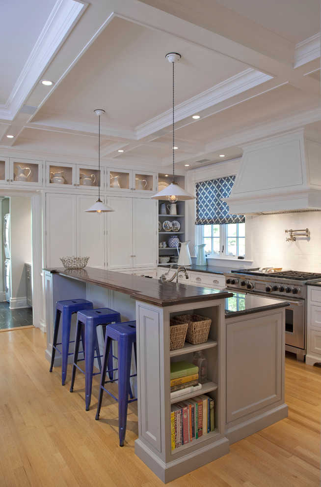 This is an example of a transitional galley kitchen in New York with shaker cabinets, white splashback, stainless steel appliances, light hardwood floors, with island and white cabinets.