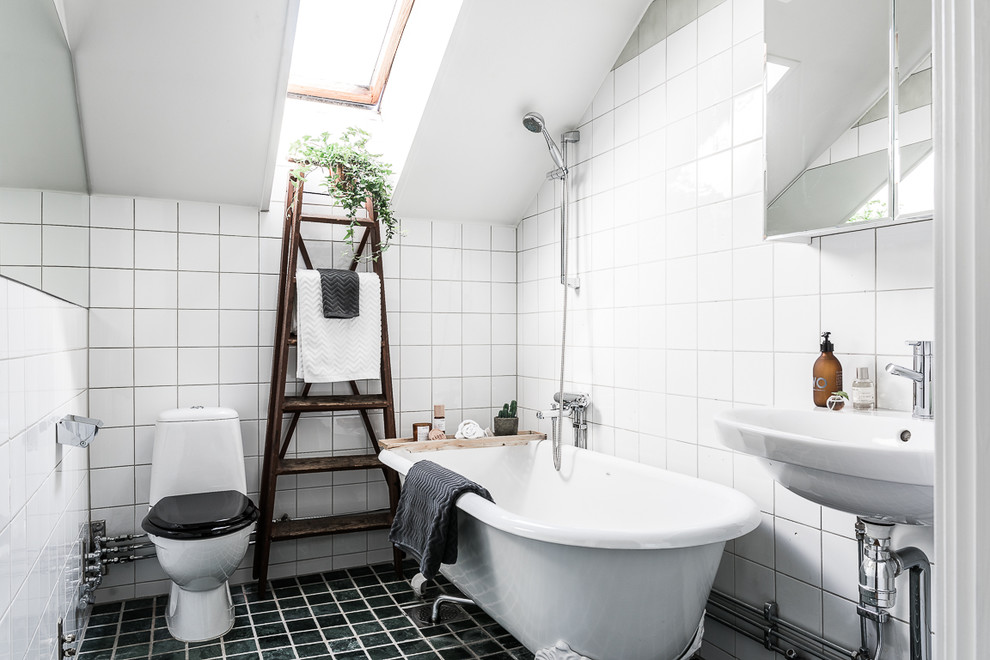 This is an example of a mid-sized scandinavian 3/4 bathroom in Stockholm with a freestanding tub, a shower/bathtub combo, white tile, white walls, a console sink, black floor and a one-piece toilet.