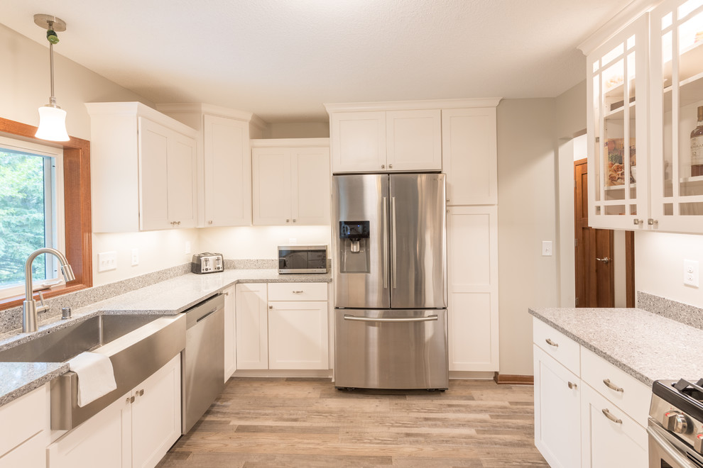Example of a large transitional u-shaped light wood floor and brown floor enclosed kitchen design in Minneapolis with a farmhouse sink, shaker cabinets, white cabinets, granite countertops, stainless steel appliances, a peninsula and gray countertops