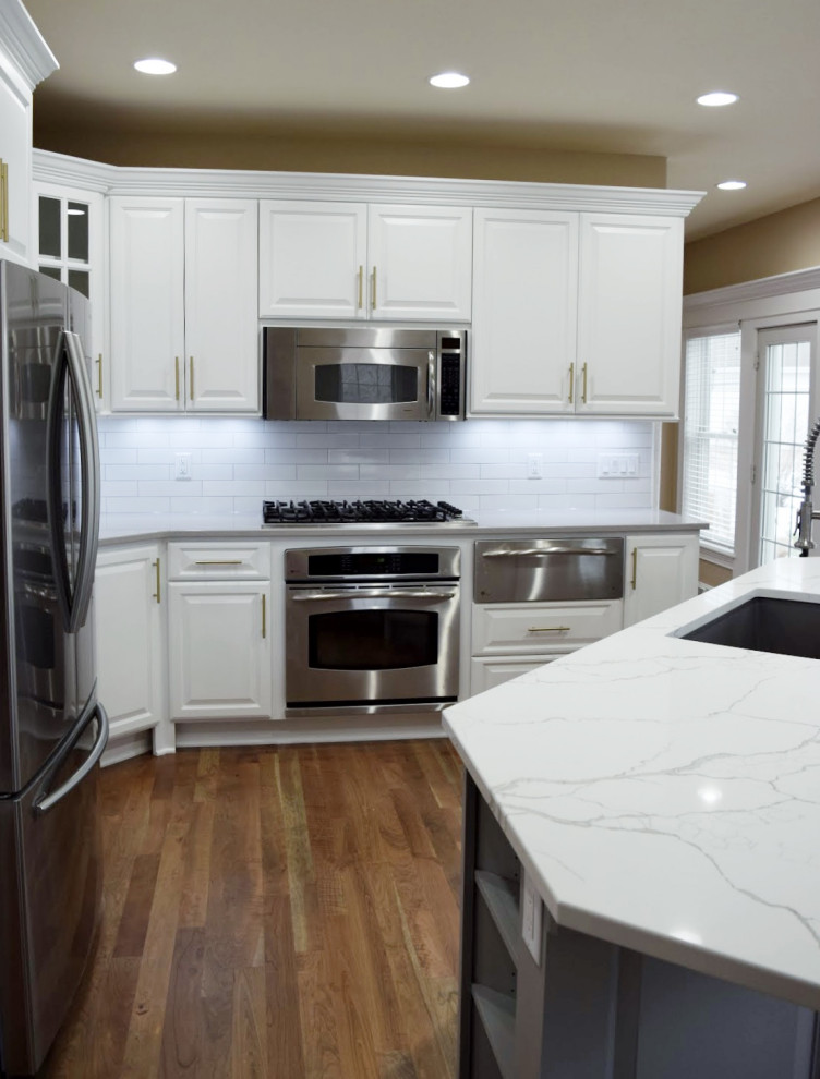 Eat-in kitchen - large transitional dark wood floor eat-in kitchen idea in Milwaukee with an undermount sink, raised-panel cabinets, white cabinets, white backsplash, stainless steel appliances and multicolored countertops