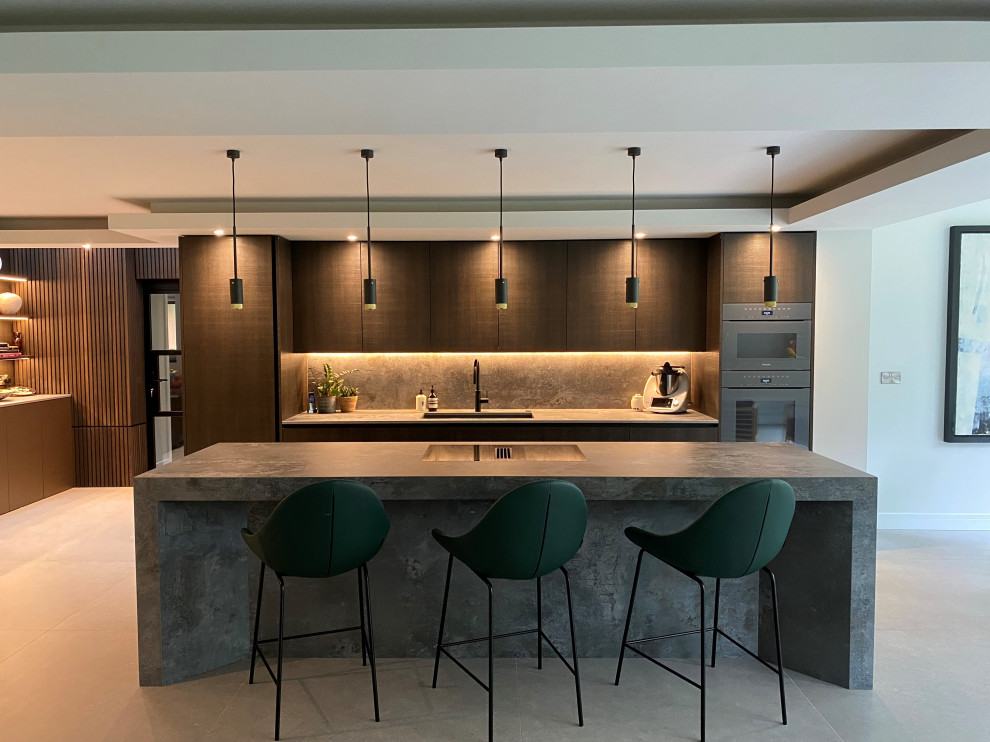 Photo of a large contemporary grey and brown galley open plan kitchen in Cheshire with a submerged sink, flat-panel cabinets, dark wood cabinets, engineered stone countertops, grey splashback, porcelain splashback, coloured appliances, porcelain flooring, an island, grey floors, grey worktops, a coffered ceiling and a feature wall.