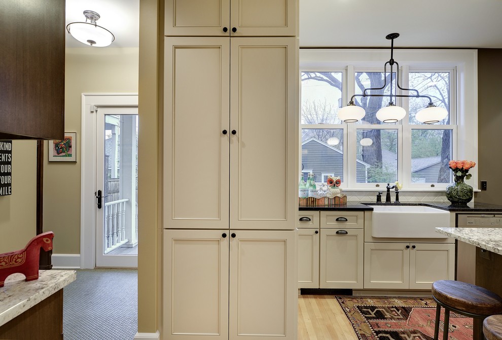 Enclosed kitchen - small transitional l-shaped light wood floor enclosed kitchen idea in Minneapolis with a farmhouse sink, recessed-panel cabinets, white cabinets, granite countertops, white backsplash, porcelain backsplash, stainless steel appliances and an island