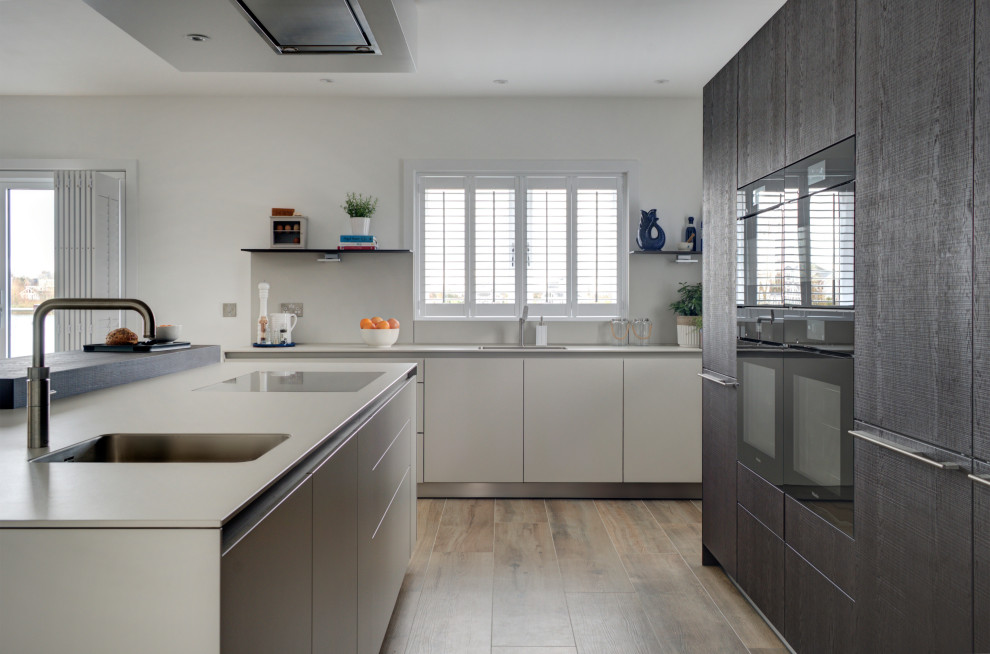 Geräumige Moderne Wohnküche in L-Form mit integriertem Waschbecken, flächenbündigen Schrankfronten, dunklen Holzschränken, Laminat-Arbeitsplatte, schwarzen Elektrogeräten, Porzellan-Bodenfliesen und Kücheninsel in Gloucestershire