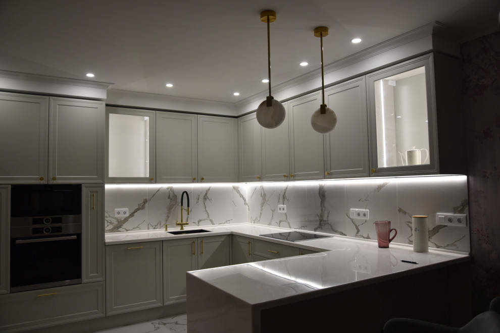 Inspiration for a large transitional l-shaped eat-in kitchen in Moscow with an undermount sink, recessed-panel cabinets, grey cabinets, solid surface benchtops, white splashback, porcelain splashback, black appliances, porcelain floors, a peninsula, white floor, white benchtop and recessed.