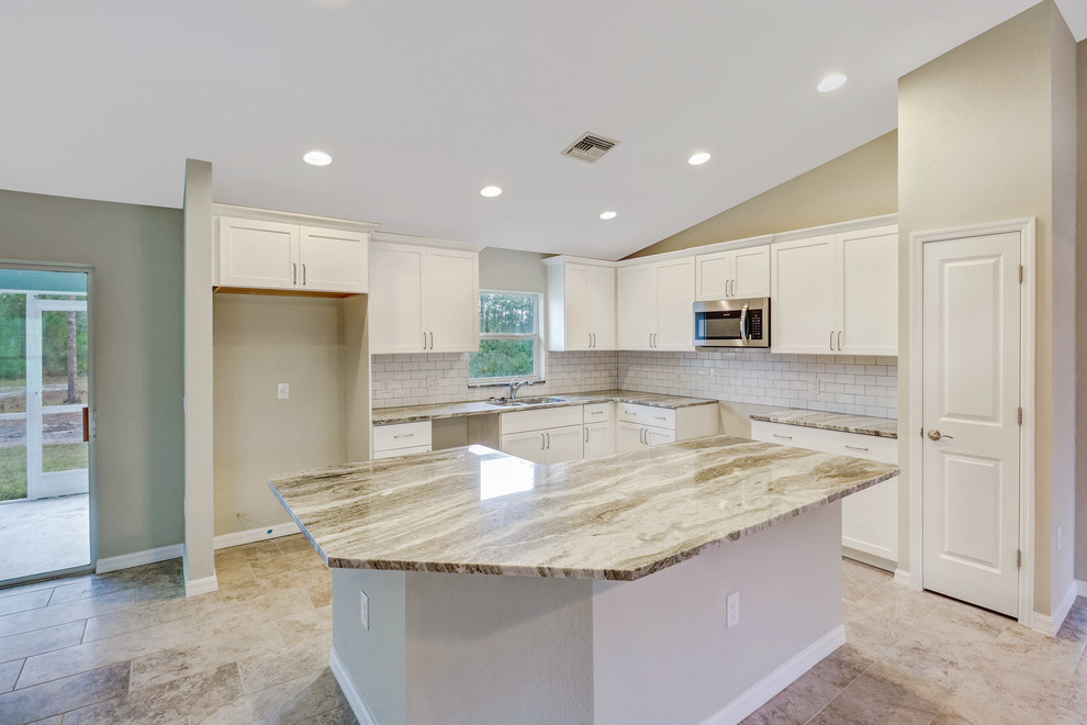 Example of a l-shaped porcelain tile and gray floor open concept kitchen design with an undermount sink, shaker cabinets, white cabinets, granite countertops, white backsplash, subway tile backsplash, stainless steel appliances and an island