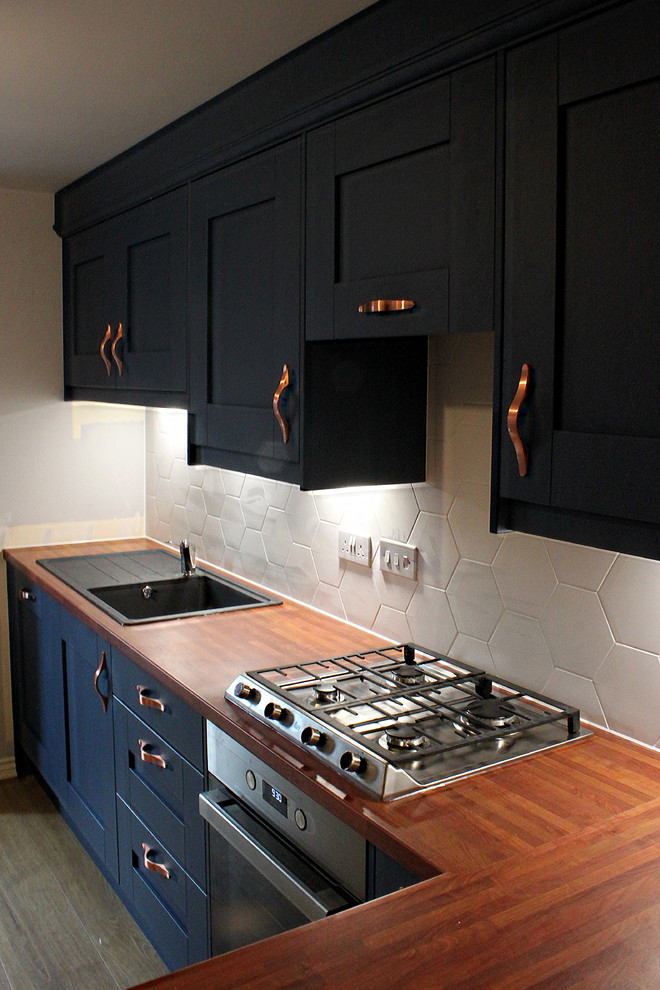 Small modern l-shaped eat-in kitchen in Cardiff with a single-bowl sink, shaker cabinets, blue cabinets, laminate benchtops, white splashback, ceramic splashback, stainless steel appliances, laminate floors, a peninsula, beige floor and red benchtop.
