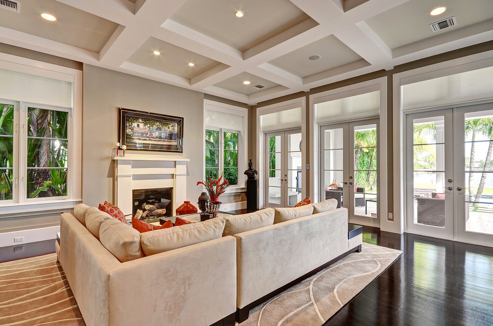 Photo of a large contemporary open concept living room in Miami with beige walls, dark hardwood floors, a standard fireplace and a wood fireplace surround.