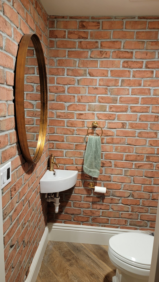 Photo of a large powder room in Salt Lake City with a two-piece toilet, vinyl floors, a wall-mount sink, a floating vanity and brick walls.