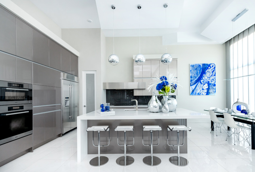 Inspiration for a large contemporary l-shaped porcelain tile and white floor eat-in kitchen remodel in Calgary with an undermount sink, flat-panel cabinets, stainless steel appliances, an island, gray cabinets, quartz countertops, gray backsplash and glass tile backsplash