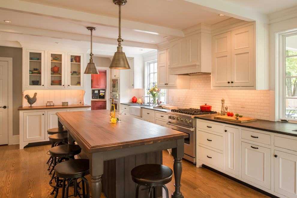 Eat-in kitchen - large traditional l-shaped medium tone wood floor eat-in kitchen idea in Philadelphia with a farmhouse sink, white cabinets, wood countertops, white backsplash, subway tile backsplash, beaded inset cabinets, stainless steel appliances and an island