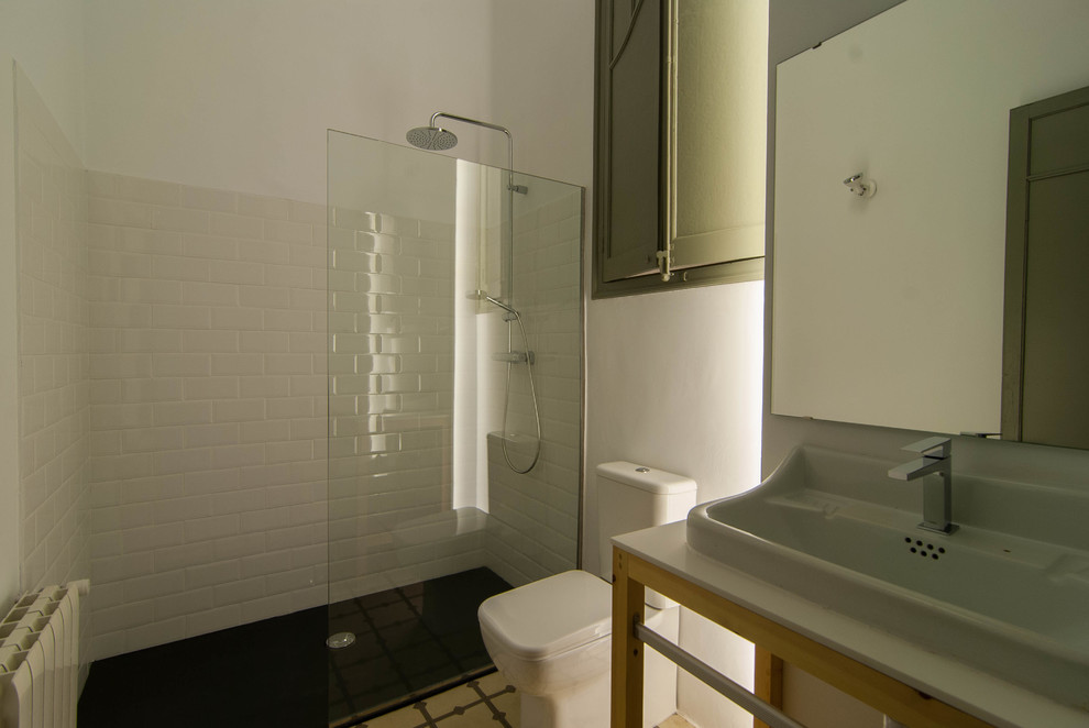 Inspiration for a mid-sized industrial 3/4 bathroom in Barcelona with open cabinets, light wood cabinets, a curbless shower, a one-piece toilet, white tile, ceramic tile, white walls, ceramic floors, a vessel sink, solid surface benchtops, multi-coloured floor, an open shower and white benchtops.