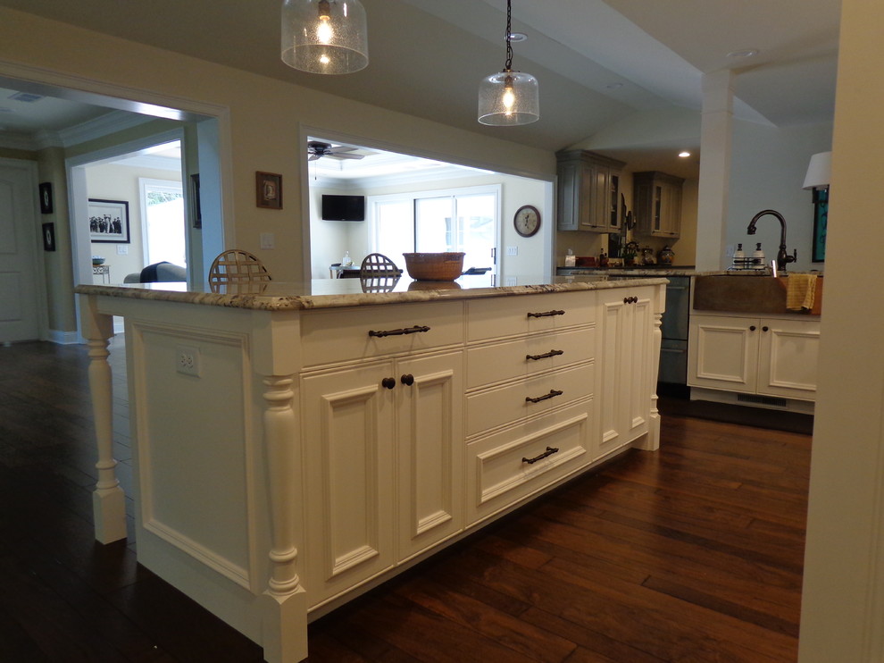 Photo of a large transitional u-shaped open plan kitchen in Raleigh with a farmhouse sink, recessed-panel cabinets, white cabinets, granite benchtops, stainless steel appliances, dark hardwood floors, with island, white splashback and subway tile splashback.