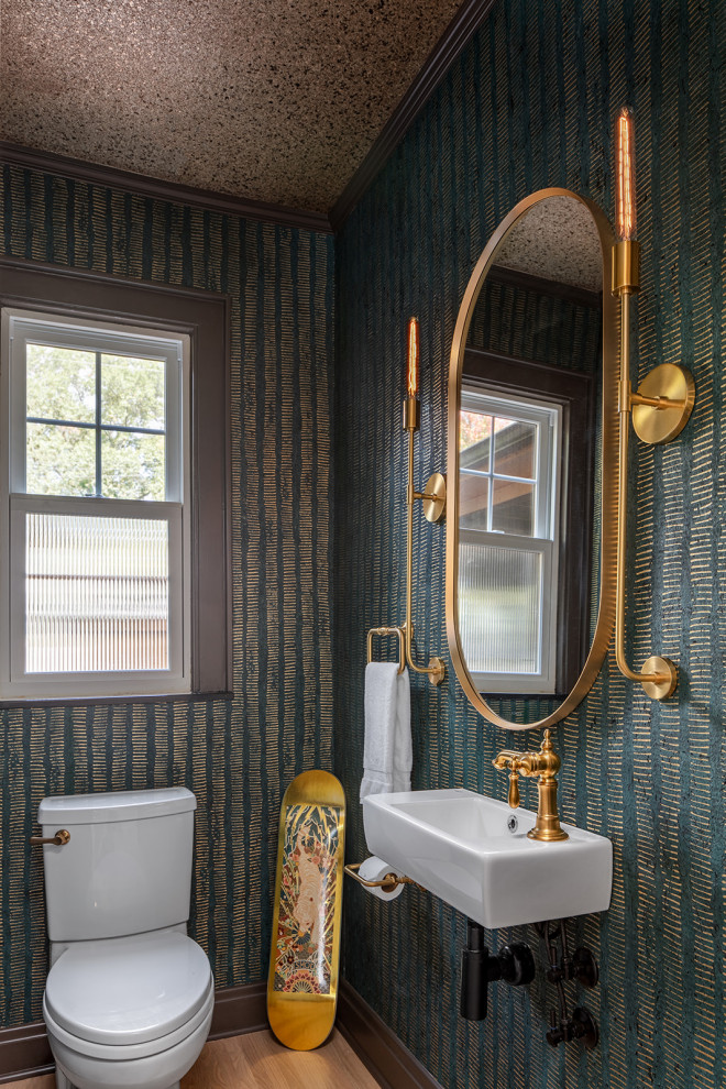 This is an example of a small transitional powder room in Columbus with a two-piece toilet, green walls, light hardwood floors, a wall-mount sink, brown floor, wallpaper and wallpaper.