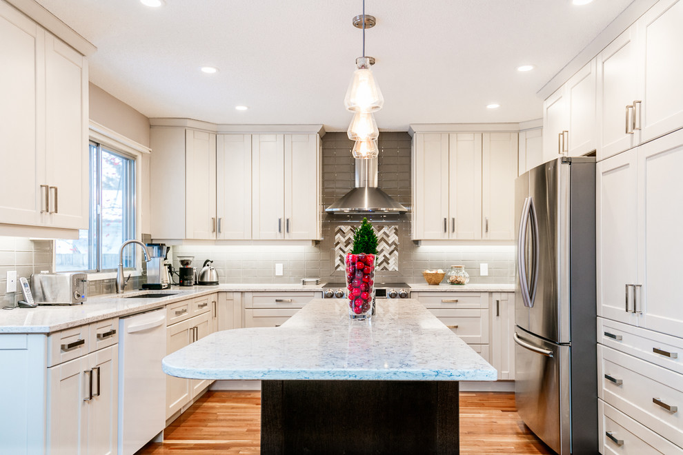 Eat-in kitchen - large transitional u-shaped medium tone wood floor eat-in kitchen idea in Calgary with an undermount sink, shaker cabinets, white cabinets, gray backsplash, glass tile backsplash, stainless steel appliances, an island and marble countertops