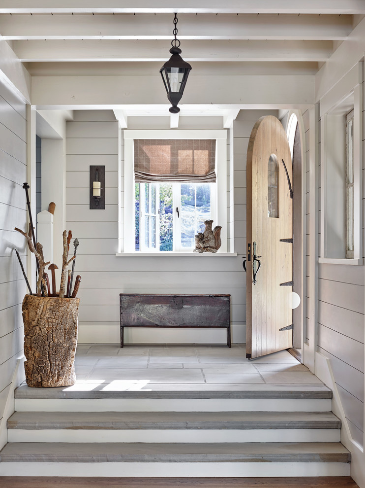 Photo of a country foyer with grey walls, a single front door, a medium wood front door and grey floor.