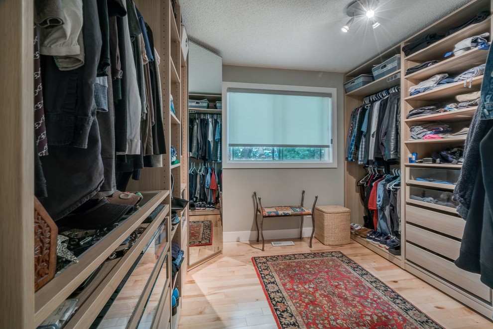 This is an example of a mid-sized midcentury gender-neutral walk-in wardrobe in Calgary with light wood cabinets and light hardwood floors.