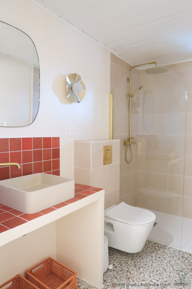 This is an example of a small mediterranean bathroom in Strasbourg with a curbless shower, a wall-mount toilet, beige tile, ceramic tile, beige walls, terrazzo floors, a drop-in sink, tile benchtops, multi-coloured floor, orange benchtops and a single vanity.