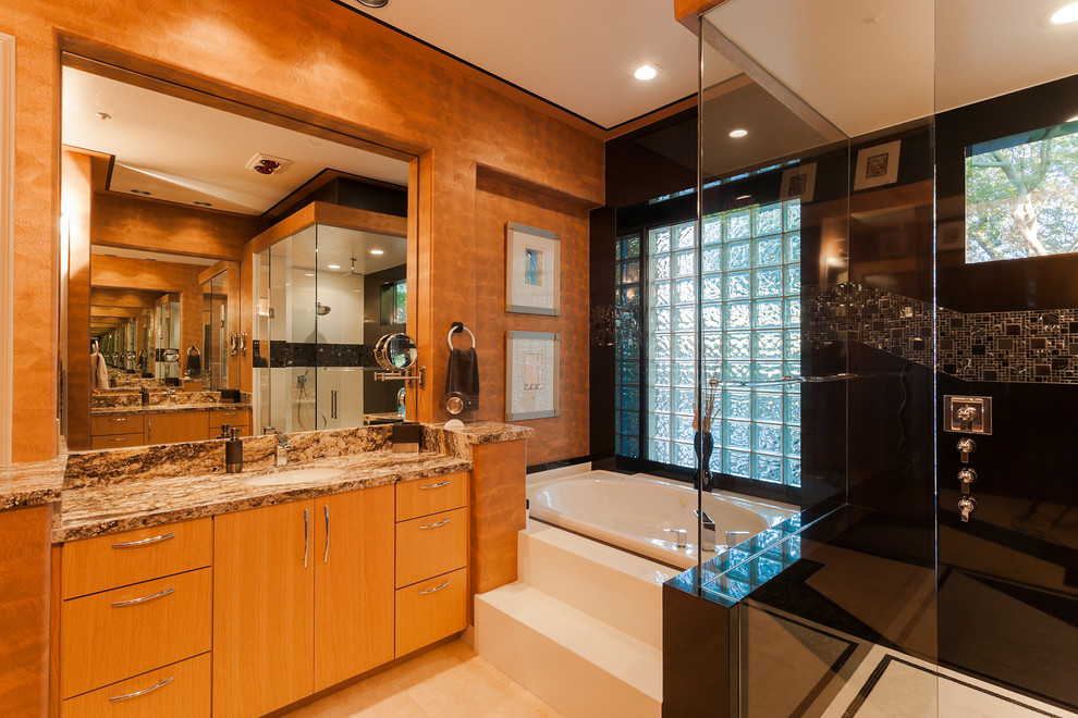 Photo of a mid-sized contemporary master bathroom in Phoenix with an undermount sink, flat-panel cabinets, light wood cabinets, granite benchtops, a drop-in tub, a double shower, a one-piece toilet, black tile, mosaic tile, multi-coloured walls and travertine floors.