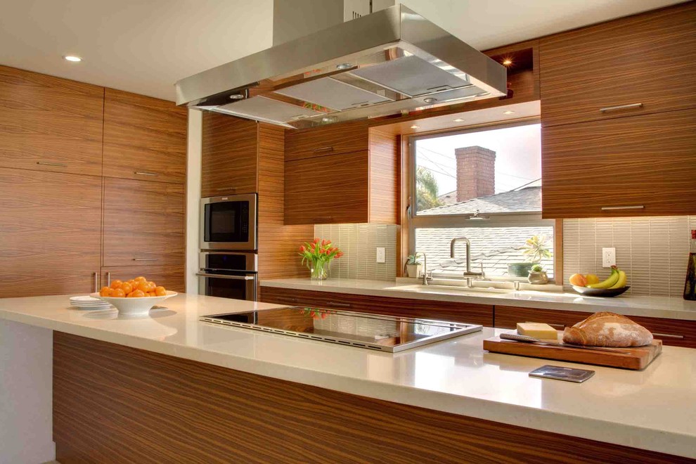 This is an example of a large modern l-shaped open plan kitchen in Los Angeles with stainless steel appliances, flat-panel cabinets, medium wood cabinets, quartz benchtops, an undermount sink, glass tile splashback, with island and porcelain floors.