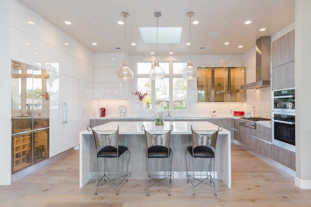This is an example of a large contemporary u-shaped open plan kitchen in San Francisco with an undermount sink, flat-panel cabinets, white cabinets, quartz benchtops, white splashback, stone slab splashback, stainless steel appliances, light hardwood floors, with island and beige floor.