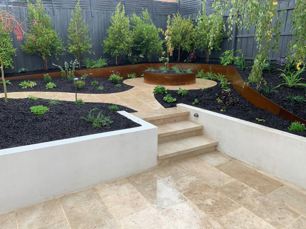 Small back partial sun garden for spring in Melbourne with a garden path, natural stone paving and a wood fence.