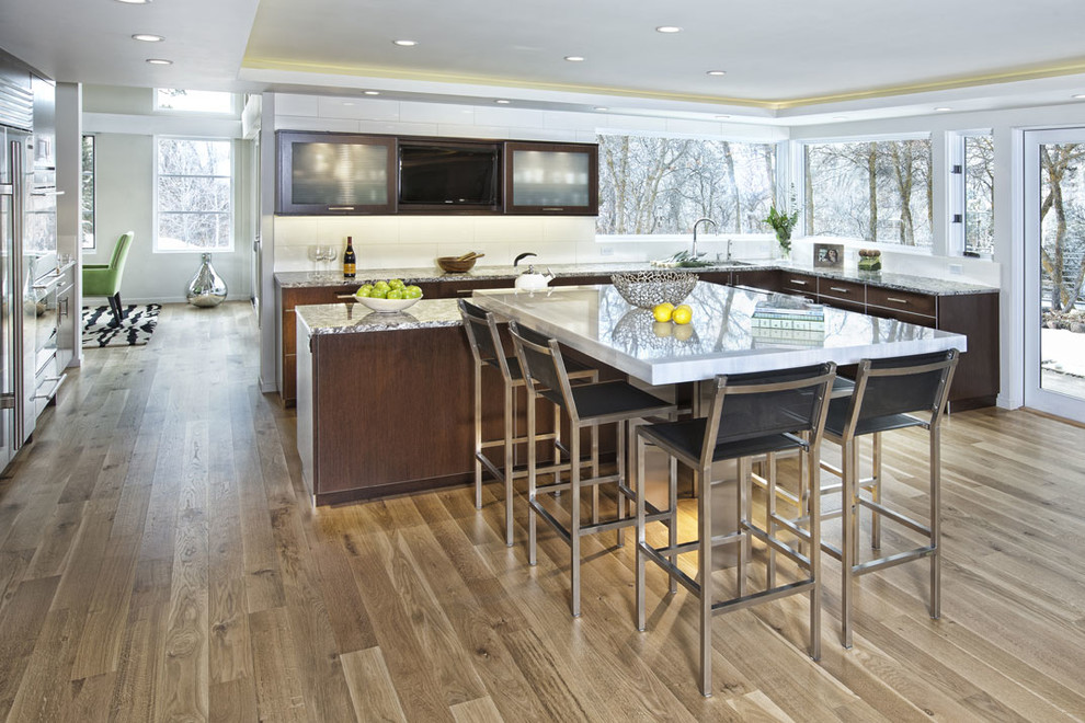 Photo of a contemporary l-shaped eat-in kitchen in Denver with flat-panel cabinets, dark wood cabinets, white splashback, an undermount sink, granite benchtops, subway tile splashback and stainless steel appliances.