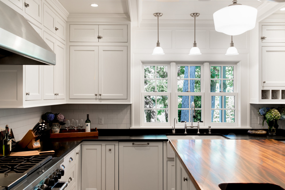 Photo of a large traditional kitchen in Portland Maine with a farmhouse sink, shaker cabinets, white cabinets, white splashback and with island.