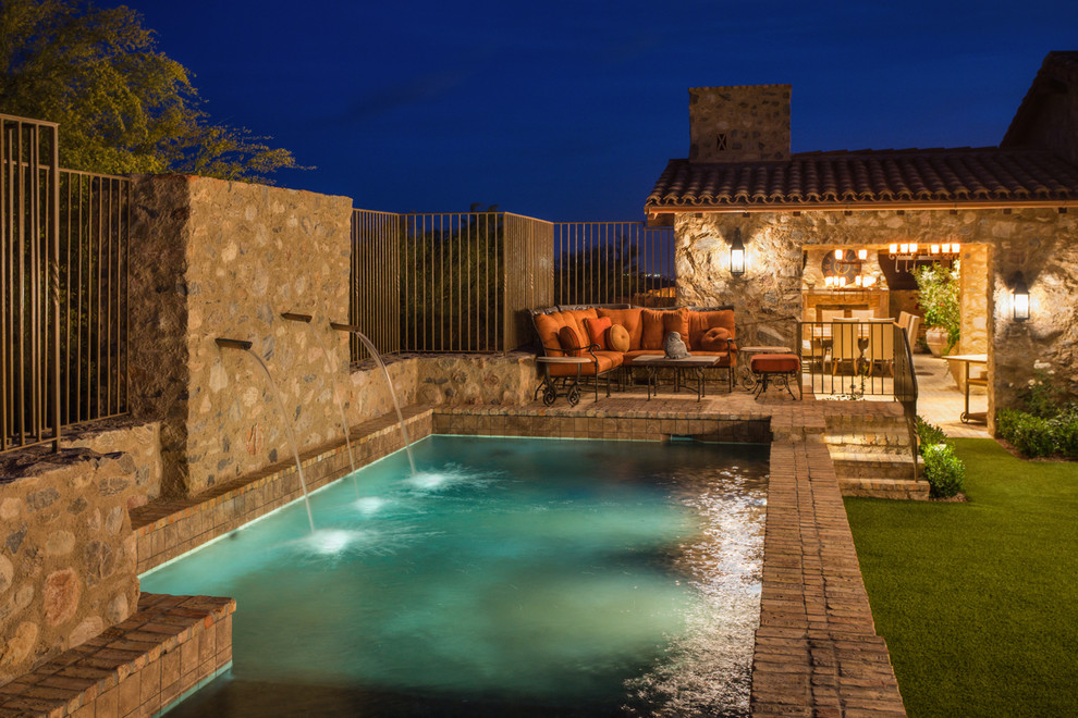Inspiration for an expansive mediterranean backyard rectangular pool in Phoenix with a water feature and brick pavers.