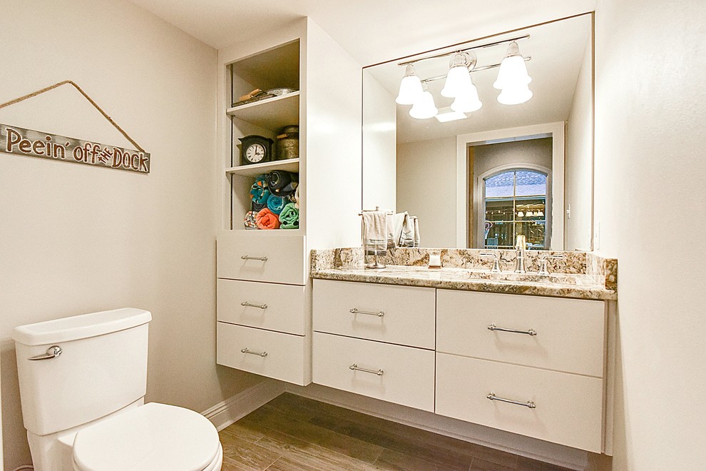 Photo of a small traditional powder room in New Orleans with flat-panel cabinets, white cabinets, a two-piece toilet, grey walls, medium hardwood floors, an undermount sink and granite benchtops.