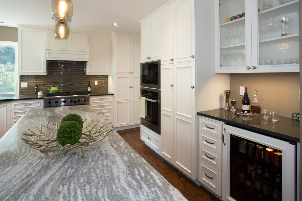 This is an example of a large traditional u-shaped open plan kitchen in Portland with an undermount sink, beaded inset cabinets, white cabinets, quartz benchtops, beige splashback, glass tile splashback, stainless steel appliances, medium hardwood floors, with island and black benchtop.