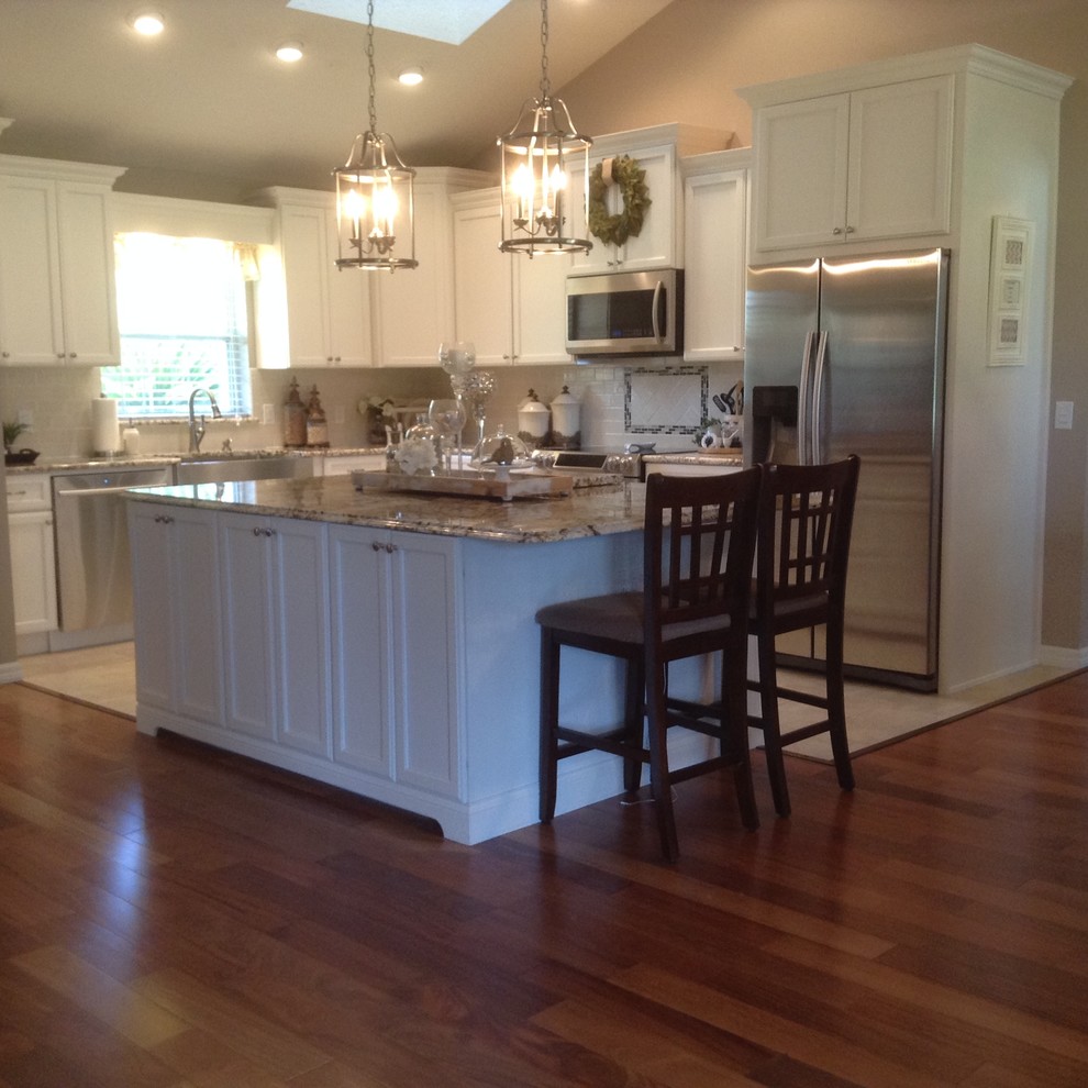 Example of a mid-sized transitional l-shaped medium tone wood floor and brown floor eat-in kitchen design in Orlando with a farmhouse sink, recessed-panel cabinets, white cabinets, granite countertops, white backsplash, subway tile backsplash, stainless steel appliances and an island
