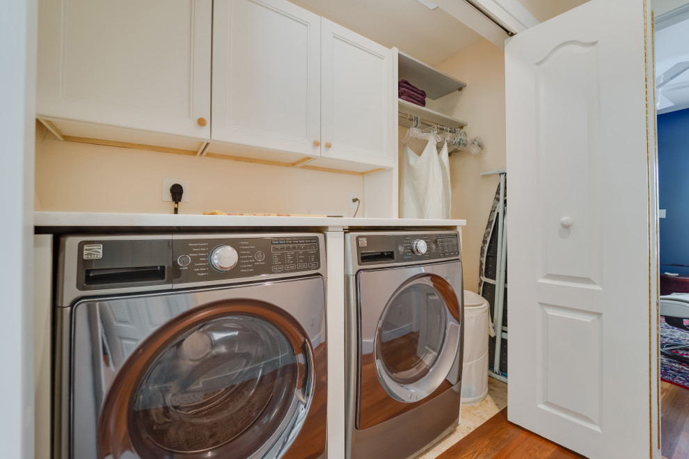 This is an example of a mid-sized country single-wall laundry cupboard in Miami with shaker cabinets, white cabinets, marble benchtops, pink walls, travertine floors, a side-by-side washer and dryer, beige floor and white benchtop.