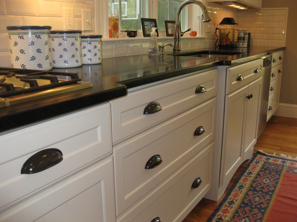 Inspiration for a transitional l-shaped medium tone wood floor eat-in kitchen remodel in Boston with an undermount sink, shaker cabinets, white cabinets, granite countertops, white backsplash, ceramic backsplash, stainless steel appliances, an island and black countertops