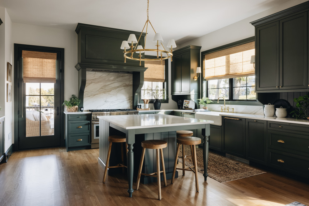 Kitchen - transitional l-shaped medium tone wood floor and brown floor kitchen idea in Chicago with a farmhouse sink, recessed-panel cabinets, green cabinets, white backsplash, stone slab backsplash, stainless steel appliances, an island and white countertops