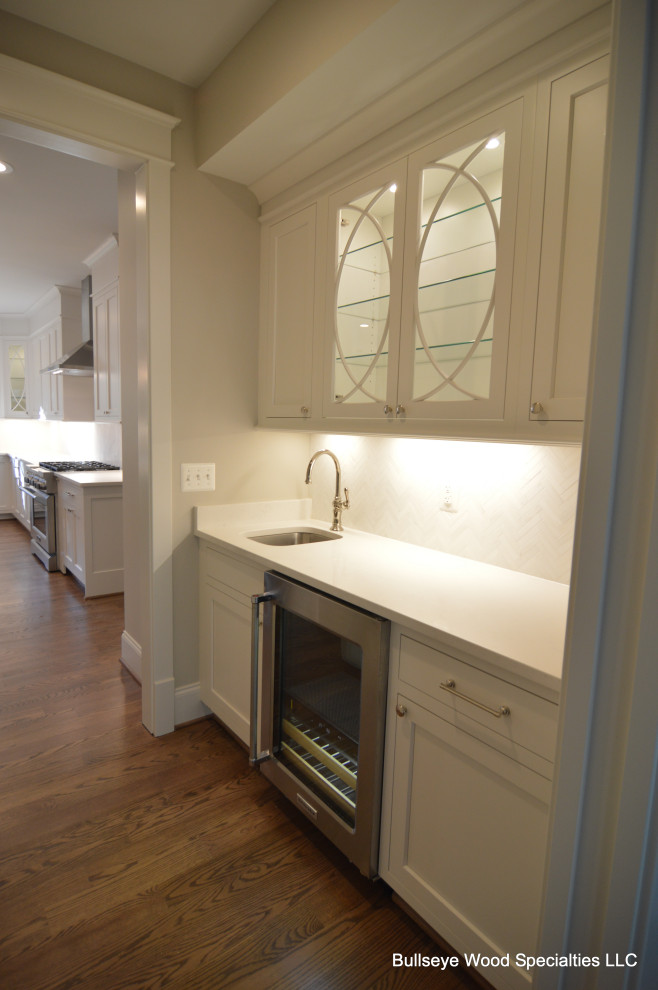 Amerikansk inredning av ett mycket stort vit vitt kök, med en undermonterad diskho, skåp i shakerstil, vita skåp, bänkskiva i kvarts, vitt stänkskydd, stänkskydd i keramik, rostfria vitvaror, mellanmörkt trägolv, en köksö och brunt golv