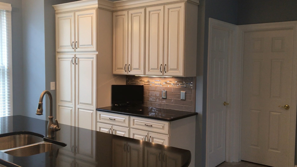 Example of a mid-sized vinyl floor kitchen design with an undermount sink, raised-panel cabinets, distressed cabinets, ceramic backsplash, stainless steel appliances and an island